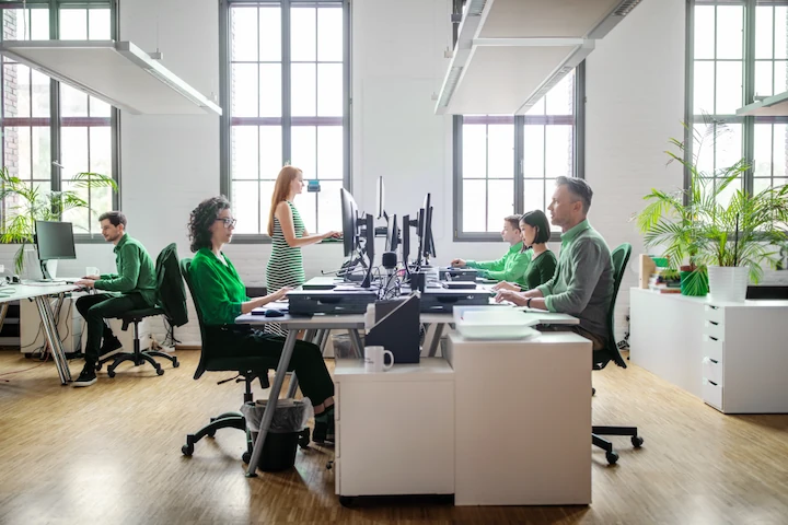 An open office with multiple people sitting at a desk in the middle of the room